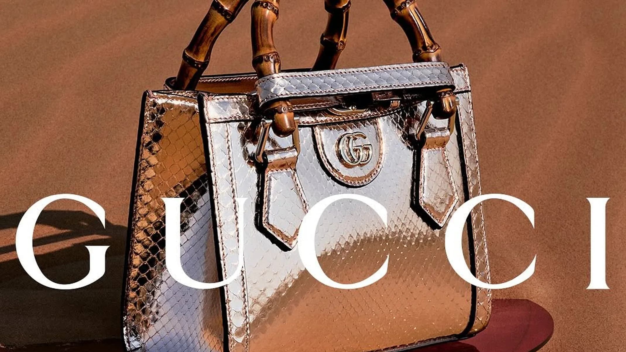 Gucci Nojum product still life of a grey textured leather clutch and small wallet on a warm desert-toned surface with a red circular accent in Sharjah Desert, UAE.
