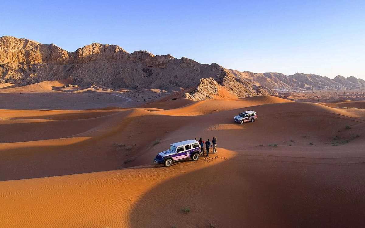 Desert landscape in the UAE with red dunes, rocky mountains, off-road vehicles, and crew on location.
