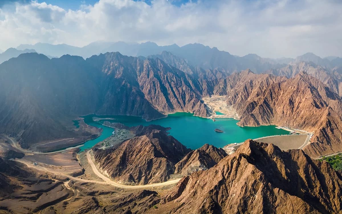 Hatta mountain landscape in Dubai with turquoise dam water, rocky peaks, roads, and dramatic highland terrain.