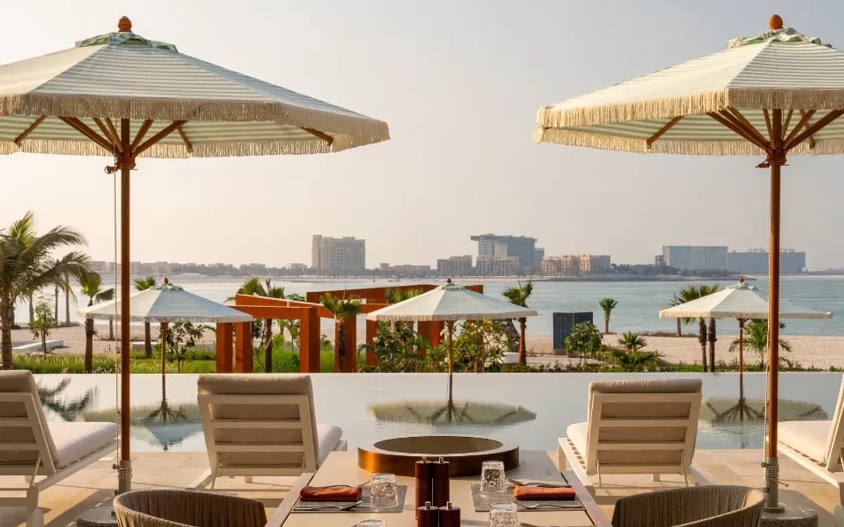 Ras Al Khaimah coastal hospitality setting with terrace seating, umbrellas, sea view, and resort skyline.