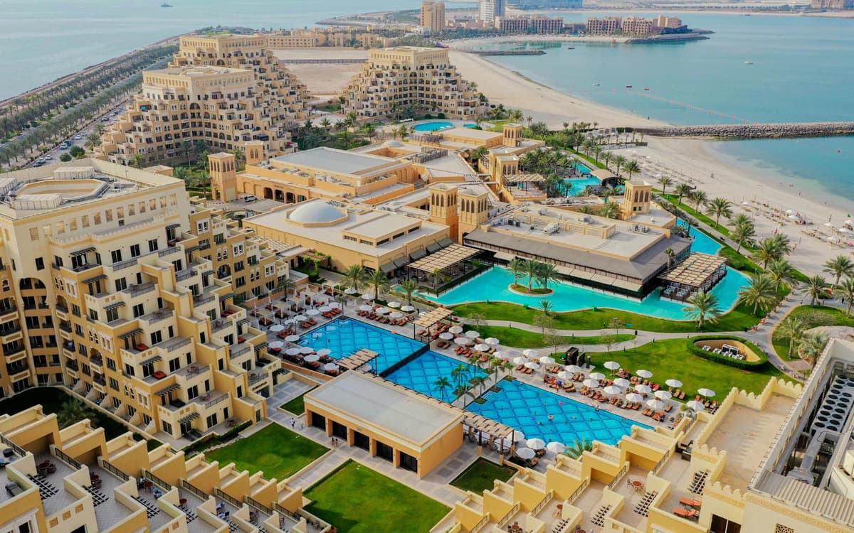 Aerial view of Ras Al Khaimah coastal resort setting with beach, pools, palm-lined grounds, and turquoise Gulf water.